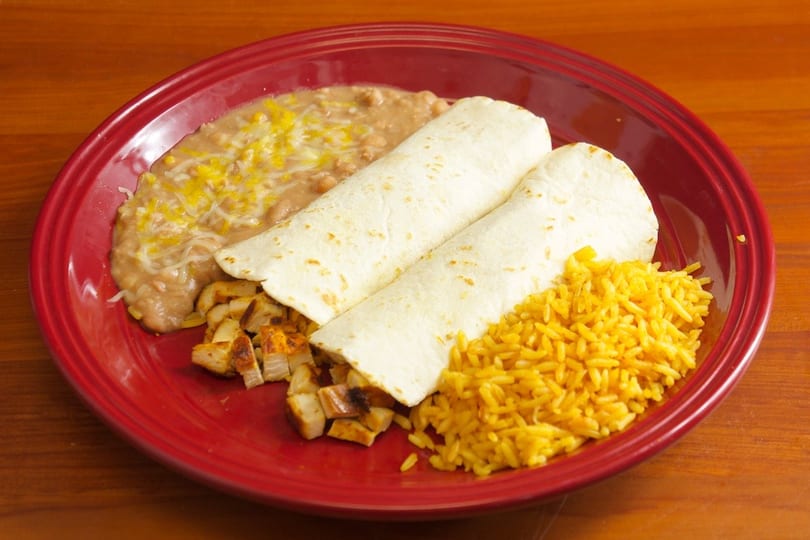 Two burritos with diced chicken, yellow rice, and refried beans with cheese on a red plate.